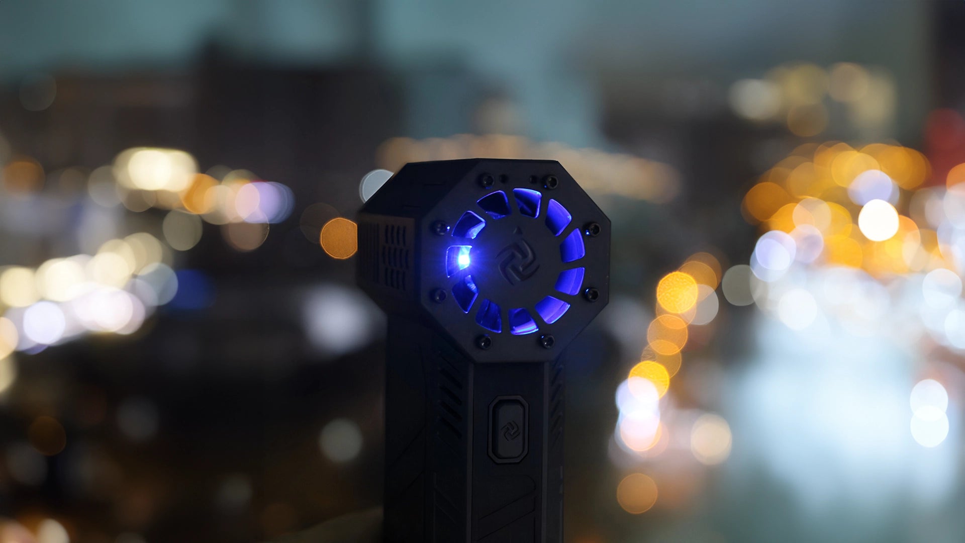 Compact jet blower with illuminated blue LED lights against a blurred city night lights backdrop, emphasizing the device's sleek design and modern aesthetic