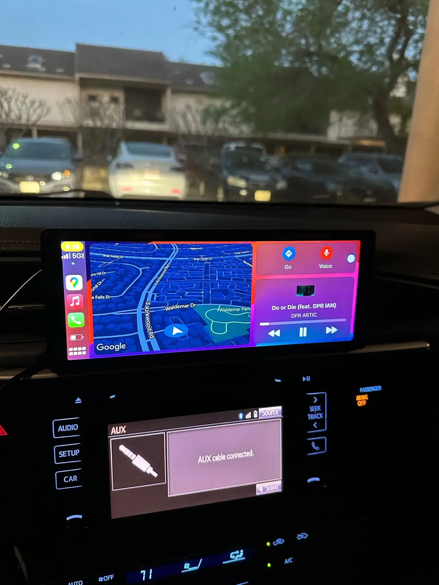 CarPlay screen showing a map and music player application above a car's built-in audio system display, captured during twilight hours